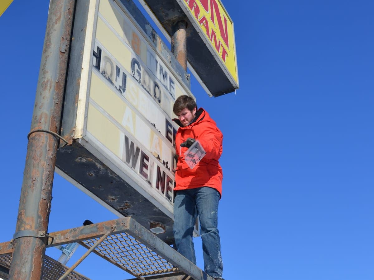 Matt Shepard on the platform of the old Horizon Inn sign, changing its letterboard message